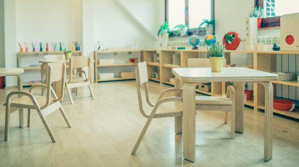Ein leerer Raum mit Tischen, Stühlen und Regalen mit Spielsachen. 