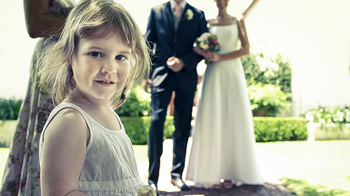Kleines Mädchen in festlichem Kleid, dahinter Hochzeitspaar. 